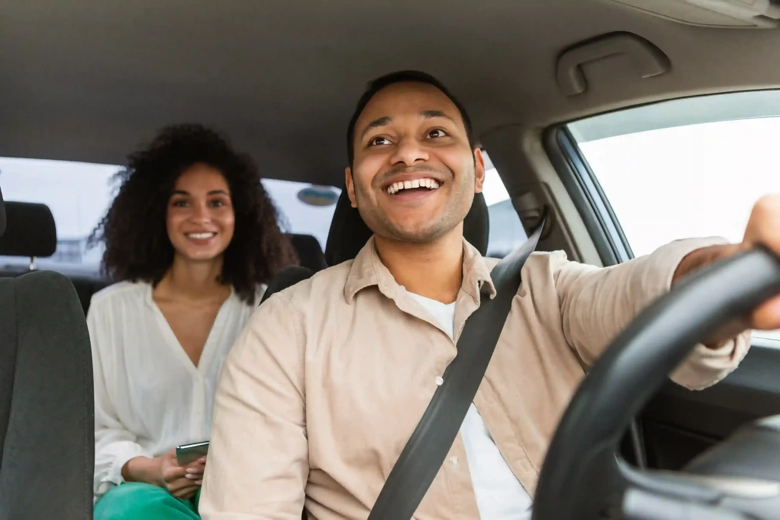 A smiling driver at the wheel with a happy rider in the back seat
